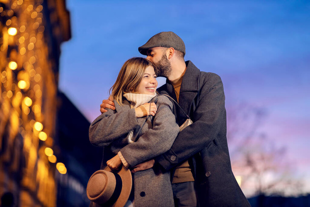 Amoureux affectueux baisers dans la rue à l'aube. Un jeune amoureux heureux debout dans la rue à l'aube et s'embrassant. Un homme étreignant sa copine et l'embrassant dans la tête. - Photo, image
