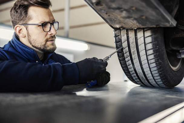 Un employé des services automobiles vérifie les pneus de voiture dans le garage. - Photo, image