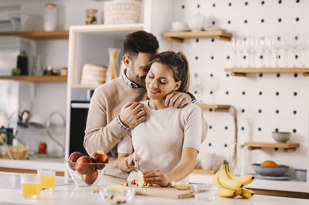 Para zakochanych obejmująca kuchnię w domu i przygotowująca sałatkę owocową. - Zdjęcie, obraz
