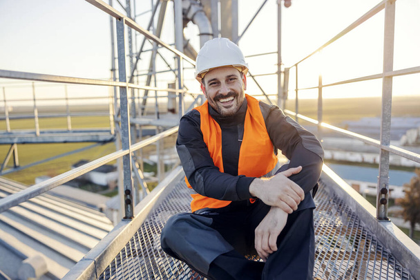 Retrato de um trabalhador de construção sentado em cima do silo e sorrindo para a câmera. - Foto, Imagem