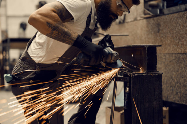 Metallurgiearbeiter hält Schleifer in der Werkstatt und schneidet Metall. - Foto, Bild