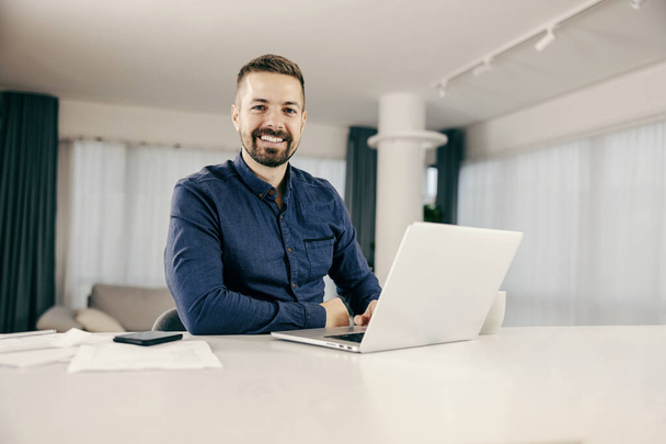 Egy boldog üzletember gépel a laptopon, otthonról dolgozik és mosolyog a kamerába.. - Fotó, kép