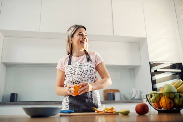 Une femme heureuse épluchant orange pour salade de fruits à la maison. - Photo, image