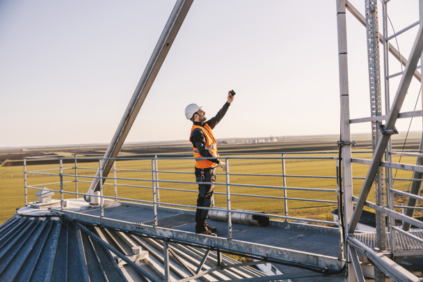 Un trabajador de la industria está parado en la construcción de metal alto y tomando selfies. - Foto, Imagen