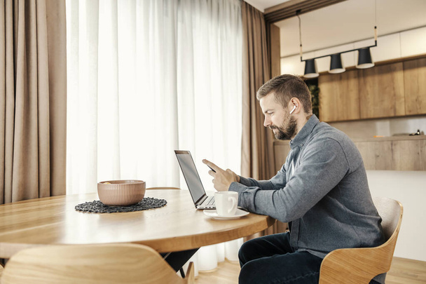 Ένας τυχαίος επιχειρηματίας κάθεται στο σπίτι και χρησιμοποιεί συσκευές υψηλής τεχνολογίας για την επικοινωνία. - Φωτογραφία, εικόνα