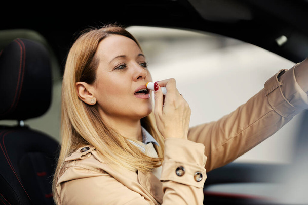Une femme à la mode met du baume à lèvres dans sa voiture. - Photo, image