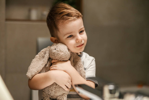 Retrato de un niño pequeño abrazando a un conejito en un baño. - Foto, imagen