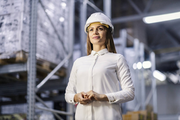 Porträt einer weiblichen CEO, die in ihrem eigenen Fabriklager steht und lächelt. - Foto, Bild