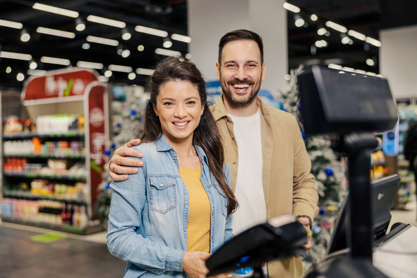 Una coppia felice è in piedi all'ipermercato alla cassa self-service e sorride alla telecamera. - Foto, immagini