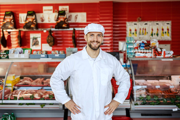 Ένας επιτυχημένος εργάτης κρεοπωλείου στέκεται σε ένα μαγαζί και χαμογελάει στην κάμερα.. - Φωτογραφία, εικόνα