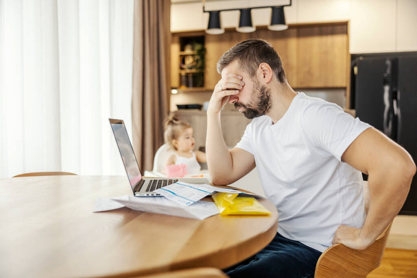A man is having headache and problems with home finances while his daughter is playing in a background. - Photo, Image