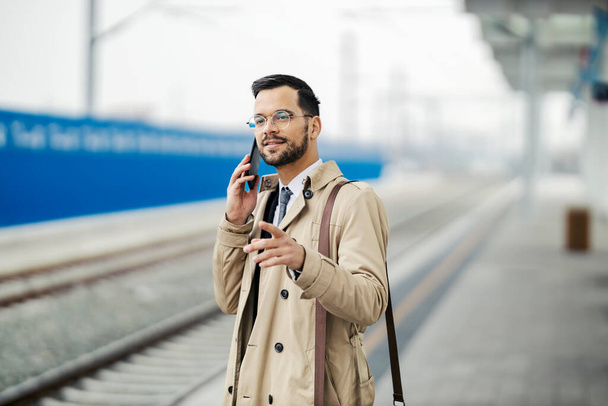 Portrait d'un jeune homme d'affaires élégant parlant au téléphone en attendant un train à la gare. - Photo, image