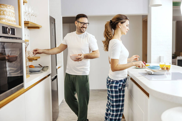 Жінка в піжамі готує сніданок, поки чоловік дивиться на неї і допомагає їй. - Фото, зображення