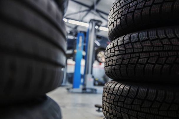 Selective focus on new tires in mechanic's shop with old ones in blurry background. - Photo, Image