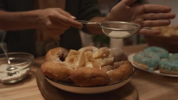 Lähikuva käsien anonyymi nuori tyttö pölyäminen donitseja ja fritters lautasen sokeri jauhe seulan avulla, kun valmistaudutaan perheen juhla - Materiaali, video