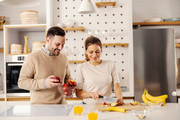 Ζευγάρι κόβει και ετοιμάζει υγιεινό σνακ, φρούτα στο σπίτι σε μια κουζίνα. - Φωτογραφία, εικόνα