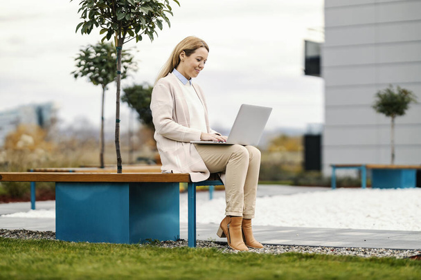A happy businesswoman in smart causal is working in a park remotely and typing on keyboard. - Photo, Image