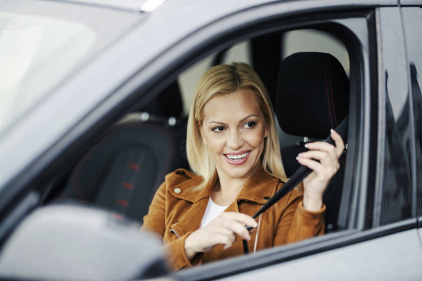 Uma mulher feliz está sentada no carro e apertando o cinto de segurança. - Foto, Imagem