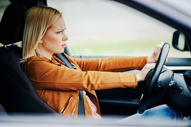 Una mujer rubia está sentada en su coche y tocando la bocina a los conductores en el tráfico. - Foto, imagen