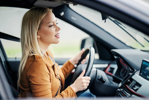 Uma mulher loira bonita está dirigindo seu carro na estrada. - Foto, Imagem
