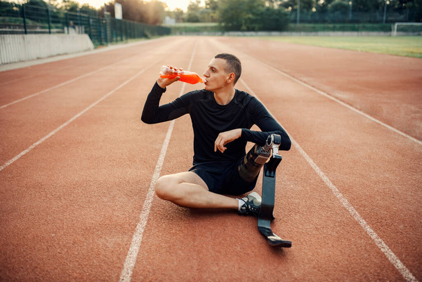 A thirsty sportsman with artificial leg sitting at stadium drinking refreshment. - Photo, Image