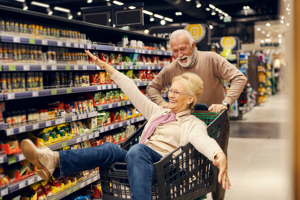 Ένα χαζό ηλικιωμένο ζευγάρι διασκεδάζει με το καροτσάκι στο σούπερ μάρκετ.. - Φωτογραφία, εικόνα