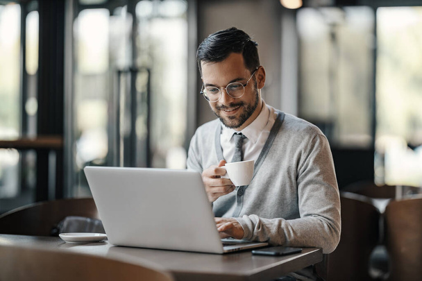 Un giovane uomo d'affari in smart casual sta bevendo caffè e digitando su un computer portatile in mensa. - Foto, immagini