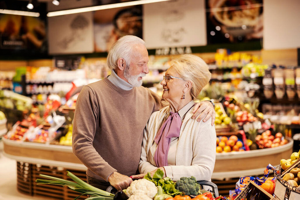 Una alegre pareja de ancianos está comprando en el supermercado y abrazándose. Mirarse a los ojos. - Foto, imagen