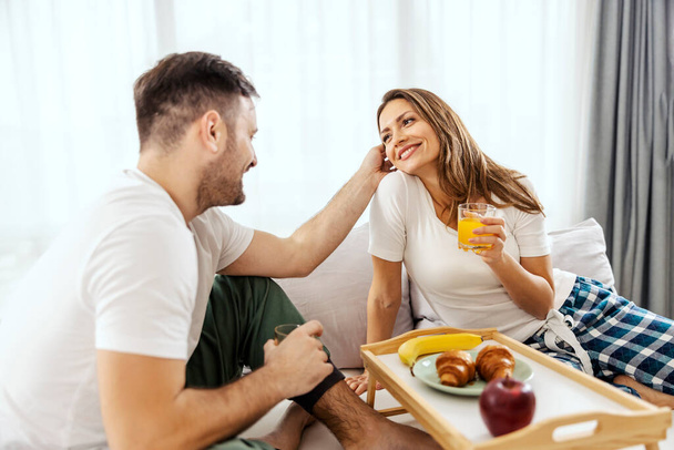 Una pareja feliz se acurruca y desayuna en una cama. - Foto, imagen