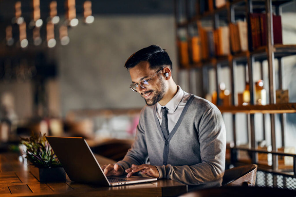 Um empresário feliz no casual inteligente está sentado no café e digitando no laptop. - Foto, Imagem