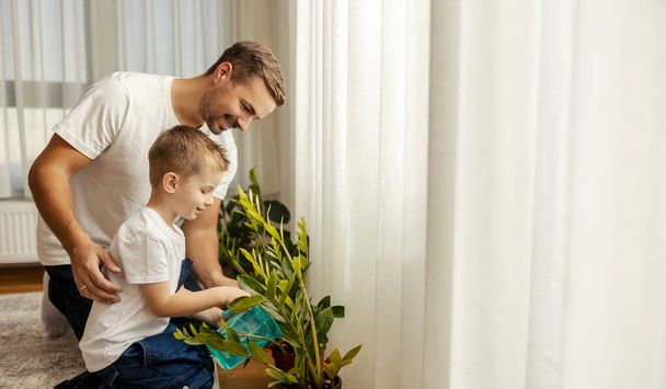 父親は子供に家事や家事をするように教えています. 男の子が家で植物を水にかけている. - 写真・画像