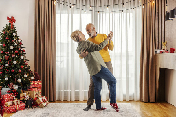 Ein verspieltes und lustiges verliebtes Seniorenpaar tanzt an Weihnachten und Neujahr zu Hause. - Foto, Bild