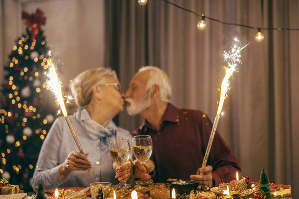 Rozmazané prarodiče líbání a slaví Vánoce a nový rok v útulném domově. - Fotografie, Obrázek