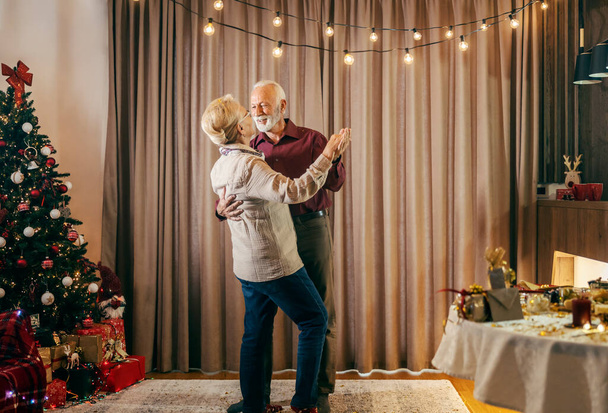 Ein festliches Seniorenpaar tanzt an Weihnachten und Silvester und feiert zu Hause. - Foto, Bild