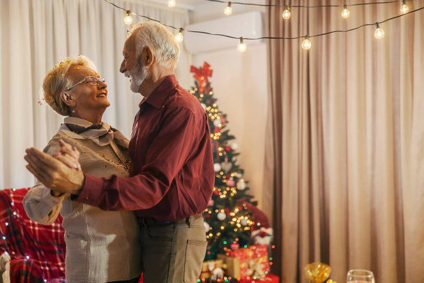 Un couple de personnes âgées affectueux danse à la maison confortable à Noël et la veille du Nouvel An. - Photo, image
