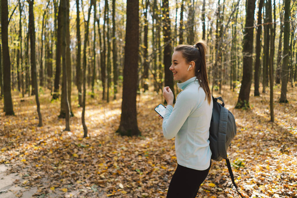 Beautiful girl listening to music and doing fitness outdoors in a sunny autumn forest. Body positive, sports for women, harmony, healthy lifestyle, self-love and wellness. - Photo, Image