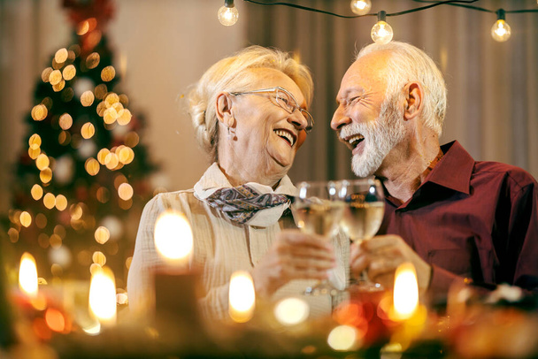 Juhlava vanhempi pariskunta maistelee viiniä viettäessään joulua ja uudenvuodenaattoa kotona.. - Valokuva, kuva