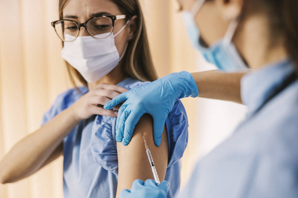 Κοντινό πλάνο μιας νοσοκόμας που κάνει εμβόλιο εποχικής γρίπης στον ώμο ενός κοριτσιού στο νοσοκομείο. - Φωτογραφία, εικόνα