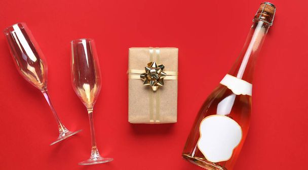 Prezent świąteczny, butelka szampana i szklanki na czerwonym tle - Zdjęcie, obraz
