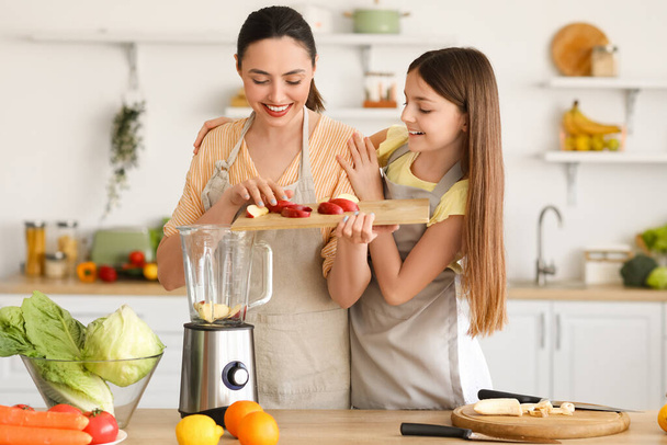 Niña con su madre poniendo manzana cortada en la licuadora en la cocina - Foto, imagen