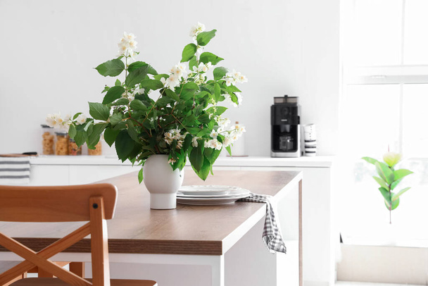 Vase with blooming jasmine flowers on wooden table in modern kitchen - Photo, Image