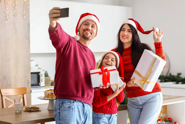 Szczęśliwa rodzina z prezentami świątecznymi biorąc selfie w kuchni - Zdjęcie, obraz