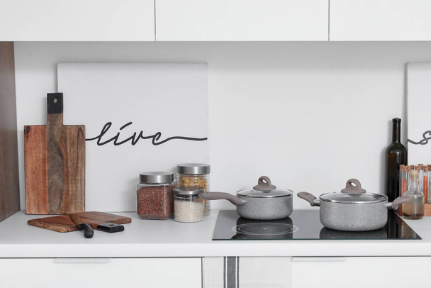 Witte keukentoonbank met elektrisch fornuis, kookpotten en keukengerei - Foto, afbeelding
