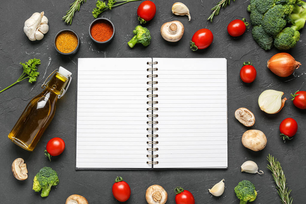 Samenstelling met blanco receptenboek, verse groenten en specerijen op donkere achtergrond - Foto, afbeelding