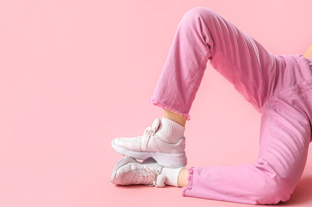 Πόδια νεαρής γυναίκας με κομψά λευκά sneakers σε ροζ φόντο - Φωτογραφία, εικόνα