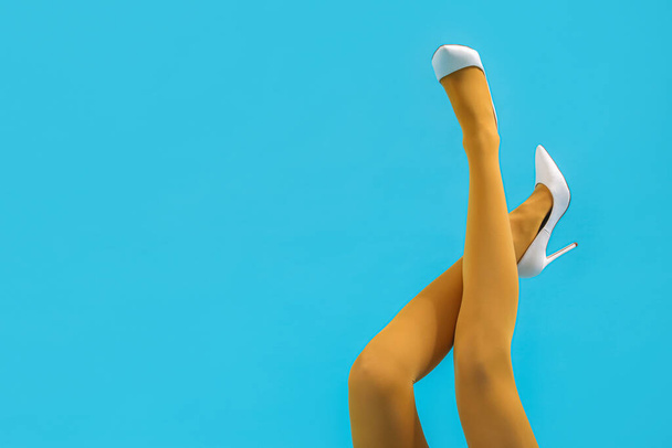 Ноги молодої жінки в стильних білих високих підборах на синьому фоні - Фото, зображення