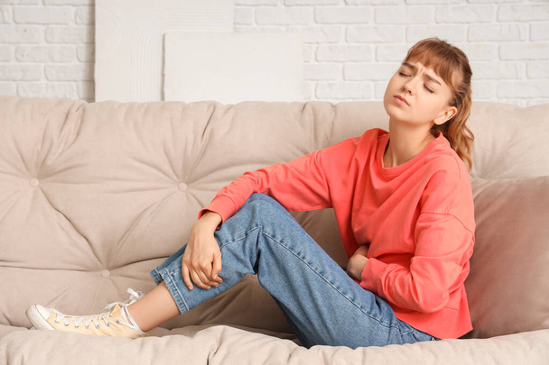 Mujer joven que sufre de dolor de estómago en el sofá en casa - Foto, imagen
