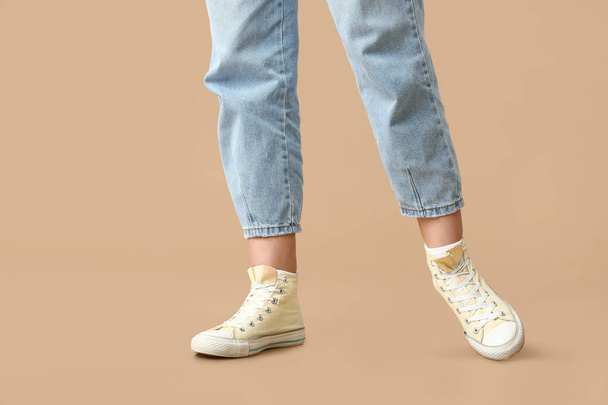 Legs of young woman in stylish sneakers on beige background - Photo, Image