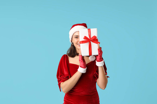 Jeune femme dans le chapeau de Père Noël avec boîte cadeau de Noël sur fond bleu - Photo, image