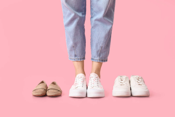 Nogi młodej kobiety w stylowych białych trampkach i różnych butach na różowym tle - Zdjęcie, obraz